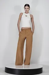 Pantalón de tiro alto color marrón, de corte ancho y silueta fluida, confeccionado en tela satinada. Presenta un detalle de ojalillos metálicos y cordón en la cintura, con bolsillos laterales.