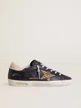 Zapatilla Golden Goose modelo Super-Star, confeccionada en cuero vacuno negro con efecto desgastado. Presenta la clásica estrella lateral de pelo con patrón animal print tipo cebra, contrafuerte en cuero nude y cordones con hilo plateado. Suela de goma con acabado envejecido y detalles con inscripciones doradas.