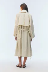 Trench coat oversize color beige, largo, con doble botonadura, solapas amplias, bolsillos laterales y cinturón ajustable para anudar.