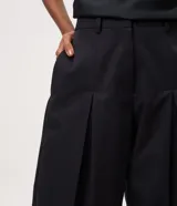 Pantalón de sarga de corte barrel, color negro, con pliegues en la cintura, piernas amplias y botamangas afinadas.
