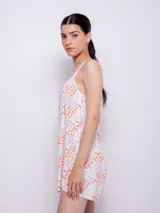 Vestido corto blanco con estampado floral en tonos naranja y lila, de corte suelto y sin mangas.