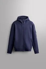 Campera canguro de Zara Athleticz, modelo relaxed fit, confeccionada en tejido técnico compacto elástico con mezcla de algodón en color azul marino. Cuenta con cuello subido con capucha, manga larga con bolsillo lateral con cierre, bolsillos frontales con cierre y acabado termofijado, cierre frontal de doble dirección y logo estampado en el bajo.
