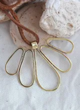 Colgante con cordón de cuero marrón y dije de metal dorado formado por figuras geométricas ovaladas.