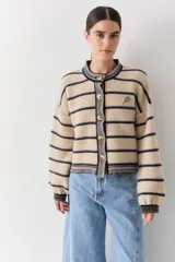 Cardigan de punto a rayas horizontales en tonos beige y azul marino, con cuello redondo, cierre frontal de botones y mangas largas abullonadas. Presenta un pequeño bordado de una raqueta de tenis en el pecho.