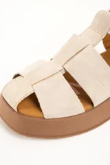 Sandalia cangrejera de cuero color beige, con plataforma baja marrón y cierre de hebilla metálica en el tobillo.