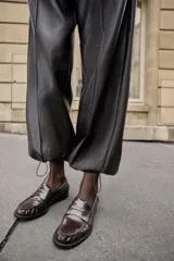 Pantalón de tiro alto confeccionado en material con efecto piel, con cintura elástica, bolsillos delanteros y nervio marcado en el frente. Presenta un diseño bombacho con bajo ajustable mediante cordones elásticos.