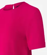 Blusa blanca de poliéster con cuello redondo, mangas cortas, cierre trasero en forma de gota, pequeñas aberturas laterales y acabados en pespuntes en las mangas y el cuello.