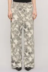 Pantalón de tiro medio y calce holgado, confeccionado en 100% algodón de peso medio con un estampado exclusivo de diseño ornamental en tonos blanco y gris oscuro. Cuenta con una cartera asimétrica cruzada en la cintura, bolsillos y sutiles desgastes manuales con pequeñas roturas localizadas.