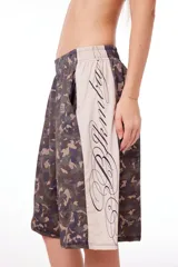 Bermuda unisex de poliéster con estampado de camuflaje y banda lateral color crema con texto en cursiva.