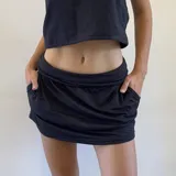 Minifalda negra con short incorporado, de diseño deportivo con cintura ajustable que permite usarla de tiro alto o bajo y bolsillos laterales.