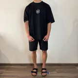 Remera negra de algodón pesado, corte oversize, con un gran estampado en la espalda en blanco y negro que muestra la parte inferior del rostro de una persona con un gorro tejido cubriendo los ojos y un cigarrillo en la boca.