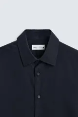 Camisa blanca de manga larga con cuello italiano y cierre frontal de botonadura. Corte regular fit.