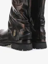 Bota corta de cuero bovino con efecto desgastado en tonos negro y gris. Presenta un diseño robusto con caña arrugada y una cremallera diagonal decorativa con tirador dorado. La suela es gruesa y dentada.