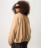 Campera bomber de sarga color beige, con diseño cortavientos, cuello alto con botones a presión y cierre frontal. Presenta mangas largas con puños elastizados, pliegues delanteros que aportan volumen y ruedo con elástico. Marca Renner.