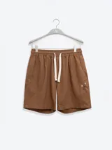 Bermuda de hombre color azul petróleo, confeccionada en mezcla de lino y algodón. Presenta cintura elástica con cordón, bolsillos laterales y trasero tipo parche. Incluye bordado floral en la pierna izquierda y etiqueta con logo en el bolsillo trasero.