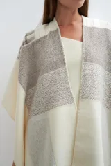 Ruana tejida con diseño de bloques en tonos tierra y beige, con cuello en V y terminación de crochet artesanal.