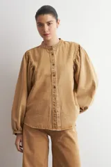 Camisa de jean color camel, de manga larga abullonada, con cuello mao y cierre frontal de botones metálicos.