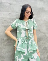 Blusa estampada con hojas verdes y blancas, con escote en V y mangas cortas abullonadas. Presenta volados en el ruedo y detalle de lazos en el frente.