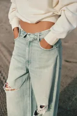 Jeans de tiro medio y corte ancho, confeccionados en denim con lavado estilo vintage de efecto desgastado. Presentan diseño de doble cinturilla superpuesta, cinco bolsillos tradicionales, trabillas para cinto y cierre frontal con cremallera y botón metálico.