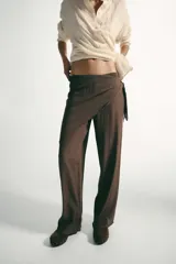 Pantalón de tiro medio con pernera recta y amplia, confeccionado en tejido con textura. Presenta una pieza superpuesta tipo pañuelo anudada en la cintura y bajo ajustable con botón.