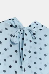 Camisa de manga larga con cuello fluido y diseño cruzado en el frente. Confeccionada en tejido semitransparente de color celeste con estampado de lunares negros. Presenta bajo asimétrico y cierre en la espalda con botones forrados.