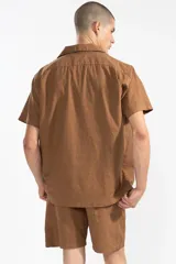 Camisa de hombre color marrón claro, de calce relajado y corte cuadrado, confeccionada en lino y algodón. Tiene cuello tipo camp, cierre con botones de coco grabados con el logo y bordado sutil de flores en el pecho izquierdo.