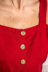 Top corto color rojo, con escote cuadrado y tirantes anchos. Presenta una hilera de botones marrones en el centro del frente.