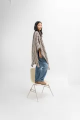 Ruana de tejido de punto con diseño a rayas horizontales en tonos beige y negro, con terminación de flecos en los bordes.