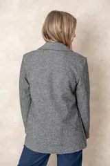 Blazer de corte sastre con diseño de espiga en tonos grises. Presenta un bordado floral lineal en el lateral, solapas clásicas, cierre frontal con un botón y bolsillos con solapa.