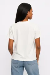 Remera de manga corta color beige, con cuello redondo y diseño de estampado floral grande en el frente.