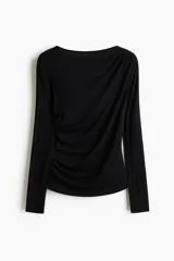 Top de manga larga de punto suave de viscosa color negro, con escote bote y diseño entallado. Presenta pliegues fruncidos en un hombro y en el lateral opuesto de la cintura para generar un efecto drapeado.