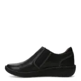 Zapatos casuales de cuero negro con cierre lateral metálico y costuras decorativas en contraste. Presentan una suela plana de goma con diseño ergonómico y forro interior en color marrón.