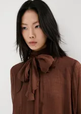 Blusa marrón de viscosa con cuello alto, volados y mangas largas acampanadas con puños elastizados.