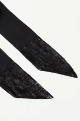 Pañuelo tipo corbatín de símil seda, color negro, con diseño largo y angosto. Presenta detalles de lentejuelas bordadas en los extremos que aportan brillo y textura.