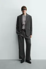 Blazer oversized fit de hombre, color gris oscuro con rayas verticales finas. Cuello con solapas de muesca, manga larga con puño abotonado, bolsillos de solapa en la cadera y bolsillo interior. Cierre frontal de un botón y abertura en el centro de la espalda.