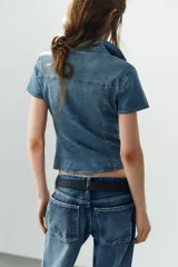 Camisa entallada de denim de manga corta, cuello camisero, bolsillos delanteros con solapa y cierre frontal de botones.