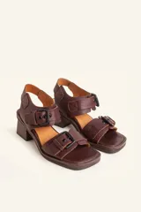Sandalias de cuero negro con taco bloque de madera tallada, tiras con hebillas grandes y punta cuadrada.