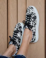 Zapatillas urbanas con estampado animal print tipo vaca en blanco y negro, con cordones negros y suela de plataforma blanca.