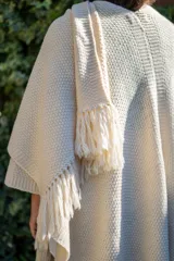 Ruana tejida a mano en punto arroz con lana merino, presenta un diseño envolvente con flecos en los extremos.