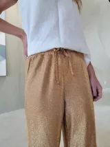 Pantalón de corte holgado y tiro medio, confeccionado en tejido brillante color dorado con acabado metalizado. Presenta cintura elástica con cordón ajustable y bolsillos laterales.