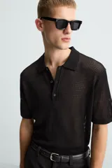 Polo de manga corta color negro, con cuello solapa y cierre frontal de botones. Confeccionado en tejido de punto con estructura abierta y calada.