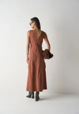 Vestido largo de sarga en color terracota, sin mangas, con escote redondo y cierre frontal completo de botones. Presenta una silueta entallada con bolsillos laterales y costuras verticales que definen el diseño.