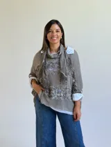 Sweater de punto color visón con diseño superpuesto, que incluye una bufanda integrada y detalles de encaje floral en el frente. Presenta mangas tres cuartos con puños abotonados y un corte holgado.