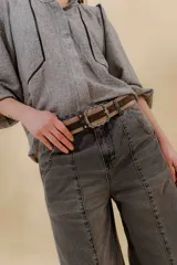Pantalón de jean gris oscuro, estilo sastrero de tiro medio bajo y corte ancho (wide leg). Presenta costuras marcadas en el frente y un cinturón trenzado marrón con hebilla metálica.
