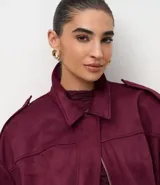 Campera bomber de gamuza sintética color bordó, con cuello clásico, cierre frontal, hombros caídos y puños ajustados.