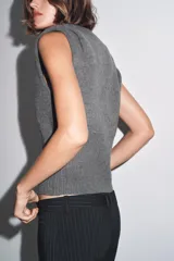 Chaleco de punto confeccionado en mezcla de lana color gris. Presenta cuello redondo, manga sisa con detalle de pliegues en los hombros y un bajo ancho en punto elástico que entalla la cintura.