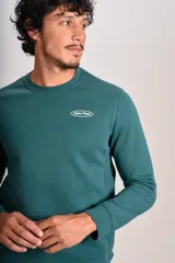 Buzo verde oscuro de cuello redondo, mangas largas con puños elásticos y pequeño estampado ovalado en el pecho.