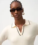 Blusa femenina de punto color blanco crema, con cuello polo y escote en V. Presenta detalles de biés negro contrastante en el cuello y los puños de las mangas largas.