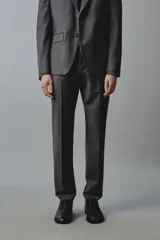 Pantalón de traje regular fit color gris oscuro, confeccionado en tejido con lana, con bolsillos frontales y bolsillos traseros de doble vivo con botón. Cierre frontal con cremallera y botón.
