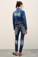 Pantalón jean de corte chupín, tiro medio y lavado azul con efecto gastado. Cuenta con bolsillos traseros con bordados ornamentales y tachas metálicas.
